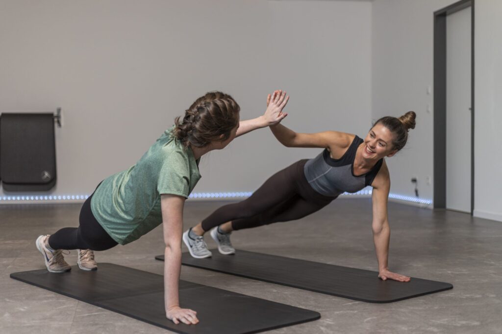 Zwei Frauen machen gemeinsam ein Fitness-Workout auf Matten und geben sich in der Plank-Position ein High-Five