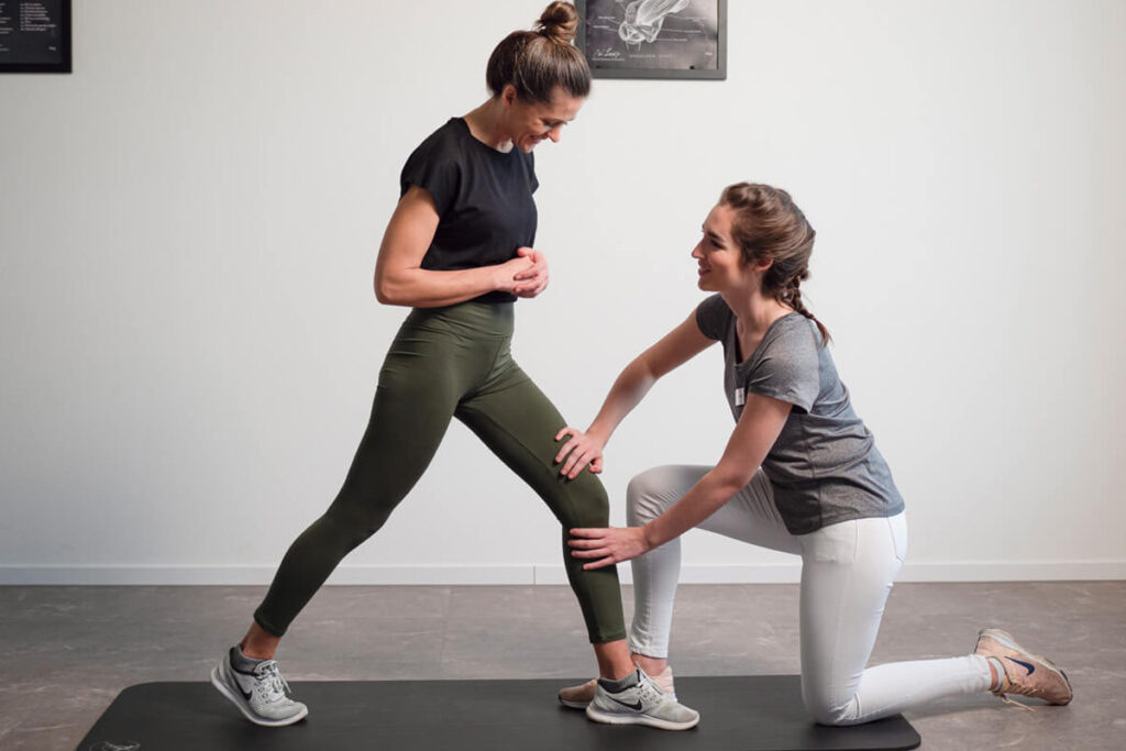 Physiotherapeutin begleitet Patientin bei einer Dehnübung auf der Matte