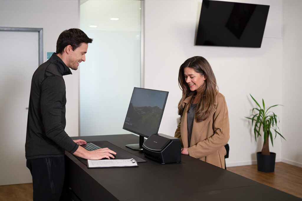 Mitarbeiter und Kundin im Gespräch am Empfangstresen einer modernen Praxis